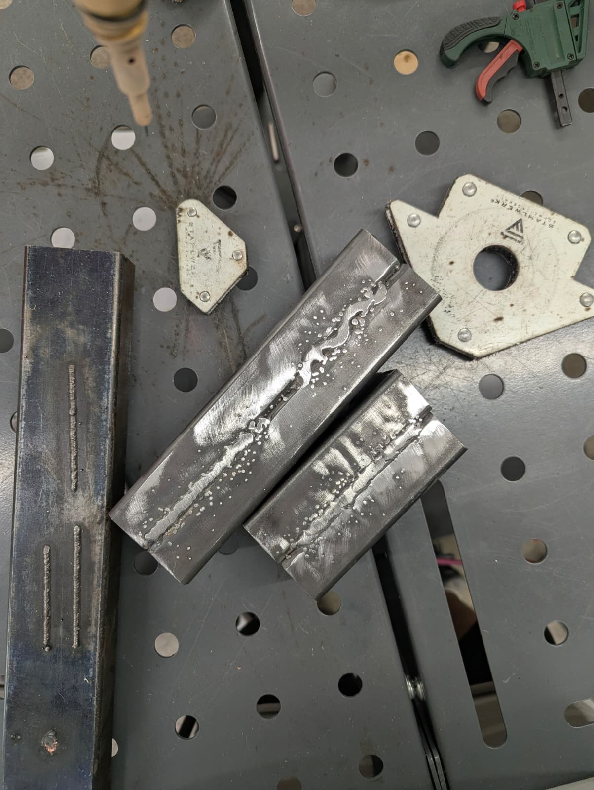 Several welded steel coupons resting on the fixture table after their passes, beads visible on each.