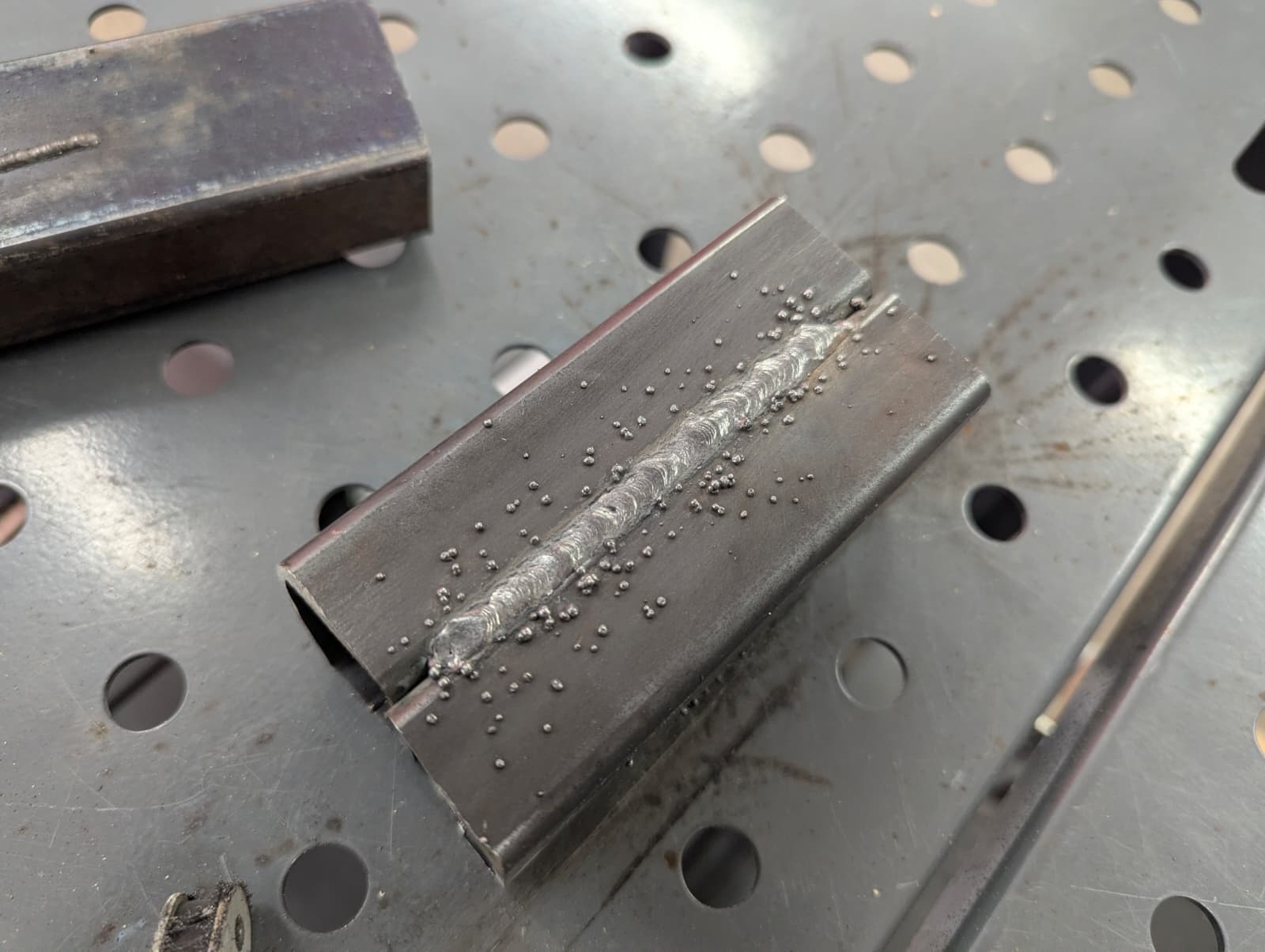 A completed weld bead running the length of a steel box section, with even ripple spacing.