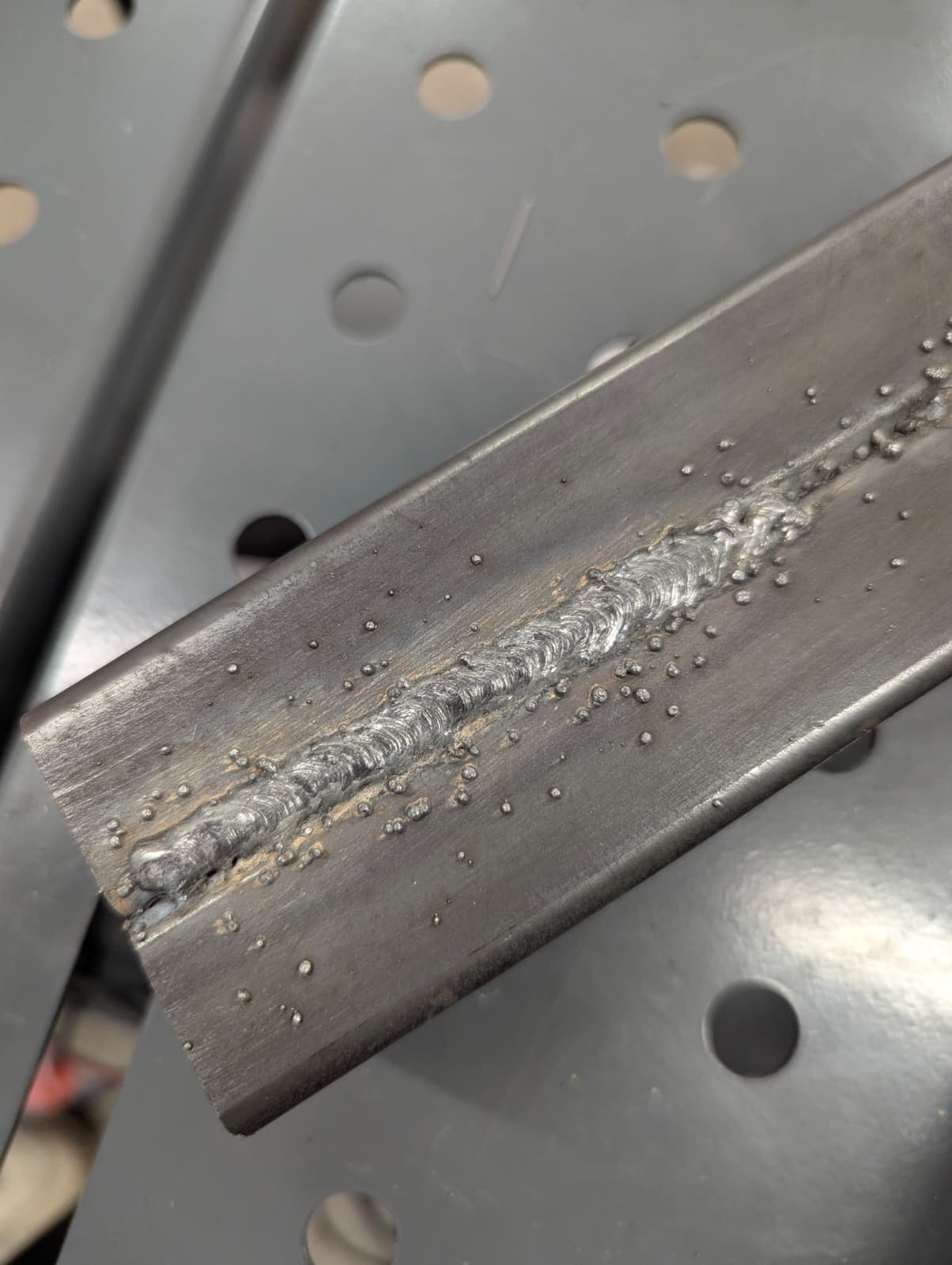 Close-up of a weld bead laid down on angle iron, showing consistent stacked ripples along the seam.
